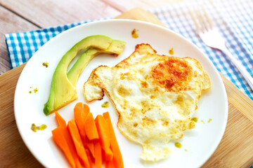 Healthy breakfast with fried egg, avocado slices and carrot sticks