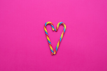 multicolored candy canes in the form of a heart on a pink background, copy space