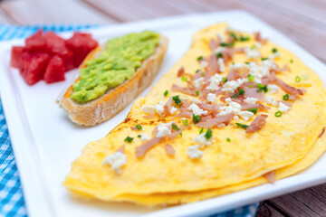 Ham and cheese omelette, toast bread with avocado and diced watermelon on square plate for breakfast.