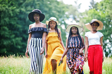 Fototapeta premium Group of four gorgeous african american womans wear summer hat spending time at green grass in park.
