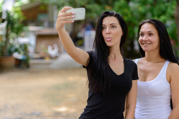 Portrait of two happy beautiful women taking selfie together outdoors