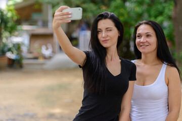 Portrait of two happy beautiful women taking selfie together outdoors