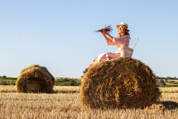 Naklejka na ściany i meble Outdoor portrait of young woman in a pink dress sitting on hay bale.