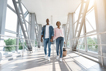 Traveling Together. Happy African Millennial Couple Walking At Airport Corridor With Suitcases