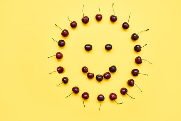 Sweet cherries in the form of the sun smiling face on yellow background