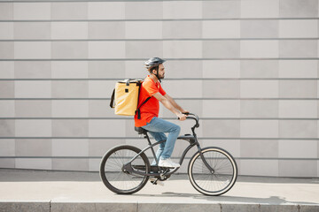 Courier cyclist on gray wall background. Young man in helmet with backpack rides on road