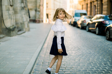 Happy little child, adorable blonde girl in black and white business wear, walking on old city street in ancient European city on sunny summer morning