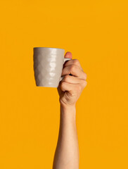 Millennial guy showing cup of hot beverage on orange background, closeup