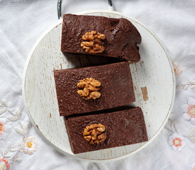 baked pieces of brownie chocolate cake with nuts on a round wooden board