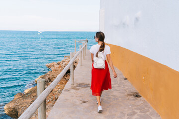 Rear view of a woman wearing a red dress on the edge of a cliff, looking at the cliffs of Las Rotas...