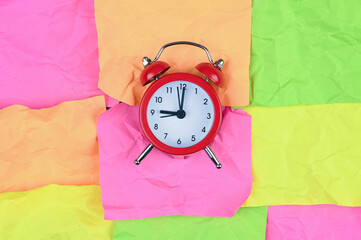 Alarm clock on multi-colored paper background.