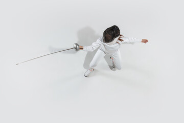 Attacking. Teen girl in fencing costume with sword in hand on white background. Top view. Young...