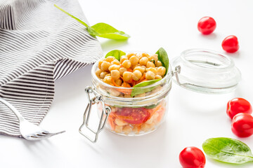 Vegan lunch. Chickpeas, carrot, tomato in glass jar on white table