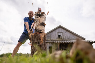 Strong man lumberjack choping wood for the winter, with a large steel ax, in the village, against...
