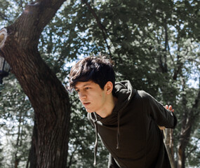 a young guy of Eastern appearance with black hair and a handsome expressive face poses in a Park against the background of trees and architecture. High quality photo