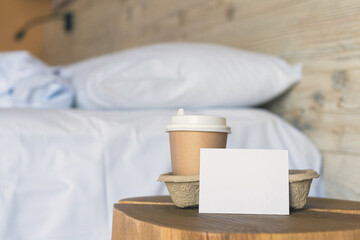 A paper cup of coffee with empty sticker for text standing on the table in the bedroom