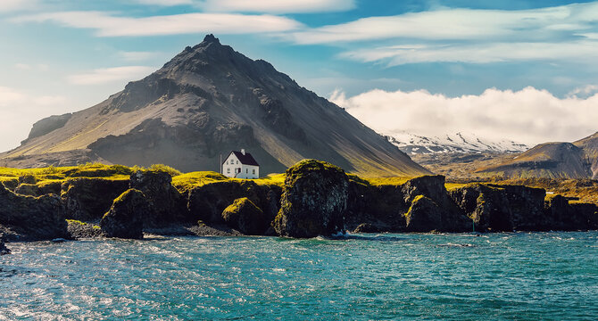 Impressive summer view at sunny day of Iceland. Wonderful nature of Iceland. Typical Icelandic landscape during sunset with houses against mountains in Arnarstapi village of at Snafellsnes Peninsula,
