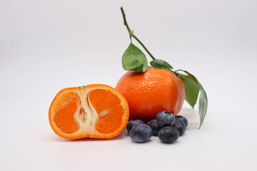 sliced tangerines with green leaves and blueberries on white background