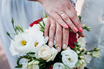 hands of newlyweds with wedding rings on wedding bouquet