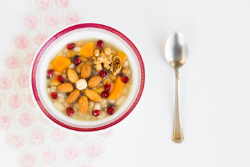 Traditional Turkish Dessert Ashure or Noah's Pudding designed flower shape in white bowl on white surface with a spoon and handmade lace cloth