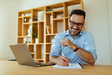 Man making notes while using laptop.