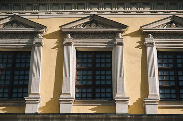 Obraz premium Windows on the facade of a house with beige plaster in the central historical part of the city. Beautiful decorative architecture with reliefs, cornice and white columns in Lviv, Ukraine.