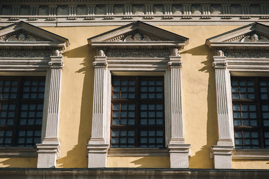 Windows on the facade of a house with beige plaster in the central historical part of the city. Beautiful decorative architecture with reliefs, cornice and white columns in Lviv, Ukraine.