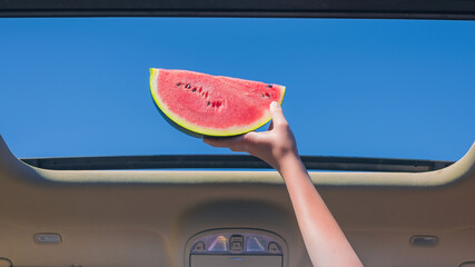 Two girls traveling by car and holding slice of watermelon in open hatch of a vehicle. Travel...