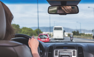 The girl is driving on the highway in Italy. View from the back seat of the car on the windshield, road and the driver