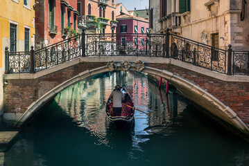 Fototapeta na wymiar A lonely gondola navigating the water channel and passing slowly below a bridge near San Marco in the center of Venice