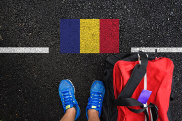 a man with a shoes and travel bag is standing on asphalt next to flag of Romania  and border