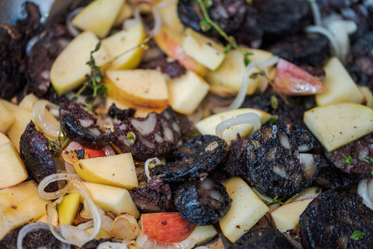 Full frame slices of blood sausage and apples mixed with onions and herbs like thyme sizzling in large frying pan
