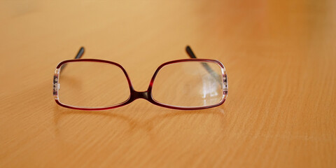 glasses with red frames lie on brown wooden table close