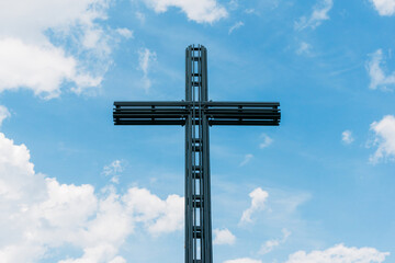 Big metal christian cross high in the blue sky. Symbol of love for Jesus. Catholic church...