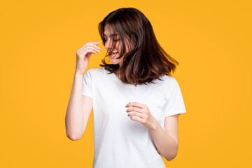 Carefree woman portrait. Fun lifestyle. Happy amused brunette lady in casual white t-shirt with fly away hair isolated on orange background. Summer joy. Positive vibe.