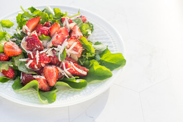 Summer salad with strawberries on a white plate and a light background. Close up. Place for copy space