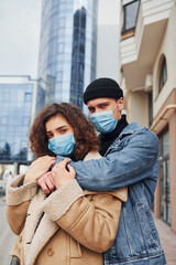 Couple in protective masks embracing each other in the city near business building at quarantine time. Conception of coronavirus