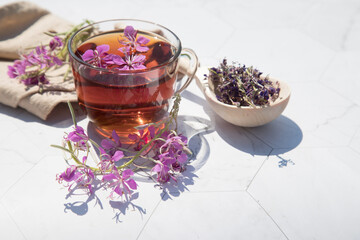Herbal tea from fermented kipreya leaves in a glass Cup on a light background, dried flowers lie in a wooden spoon next to it.Traditional Russian Kopor Tea (Ivan-Tea). Place for a copy of space