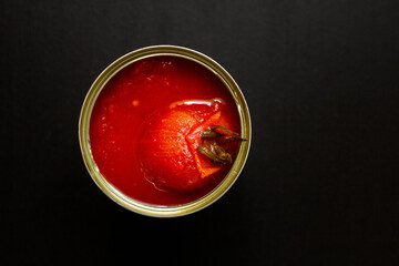 Opened tin can of tomato sauce with one whole tomato on top. San Marzano (italian plum tomato) ingredient for authentic Pizza Napoletana (true Neapolitan Pizza). From above on black background.