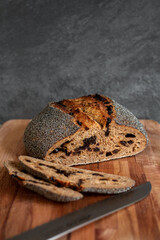 Fresh baked, hand crafted artisan sourdough bread. Deliciously organic rustic wholegrain spelt loaf covered in poppy seeds with raisins inside. Healthy cooking at home. Grey concrete wall background.