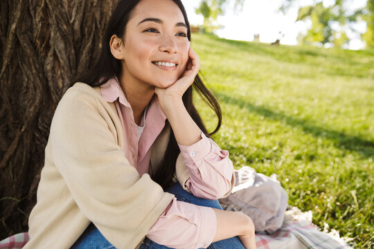 Image of joyful asian student woman resting while sitting on grass