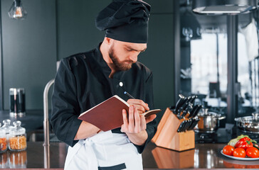 Professional young chef cook in uniform standing with notepad on the kitchen