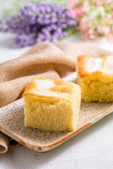 A piece of square coconut cake on plate and white table. Homemade delicious bakery.