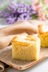 A piece of square coconut cake on plate and white table. Homemade delicious bakery.