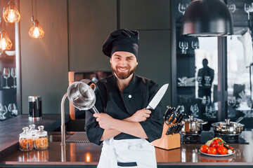 Professional young chef cook in uniform standing near table and posing for a camera on the kitchen