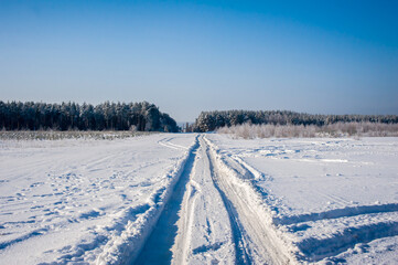 Fototapeta na wymiar Winter road in deep snow in winter. Through the field to the pine forest. Clear sunny day.
