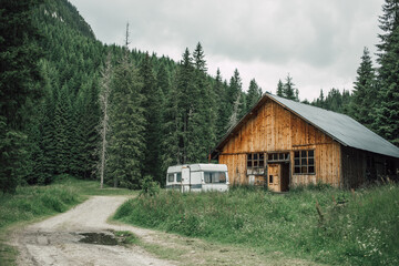 Abandoned camper van and rustic chalet on a mountain trail in the woods. Country style home in the mountainside. Outdoors lifestyle. 