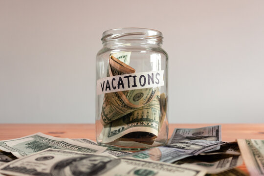 Money US Dollar bills in a glass jar labeled "vacations". Saving financial concept