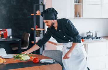 Professional young chef cook in uniform making salad on the kitchen