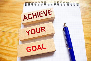 Achieve your goal words on wooden blocks on notepad with blue pen on wooden background.